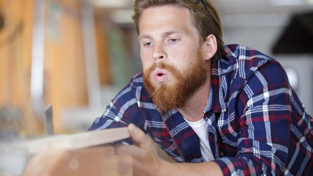 carpenter blowing dust from piece of wood
