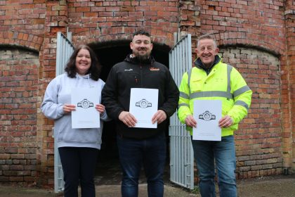 A group photo of Caroline Platt, Paul Gorshwin, and John Tabern standing together at the Cannington Shaw site, representing the leadership and craft expertise behind the new Community Shed project