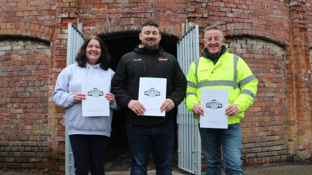 A group photo of Caroline Platt, Paul Gorshwin, and John Tabern standing together at the Cannington Shaw site, representing the leadership and craft expertise behind the new Community Shed project